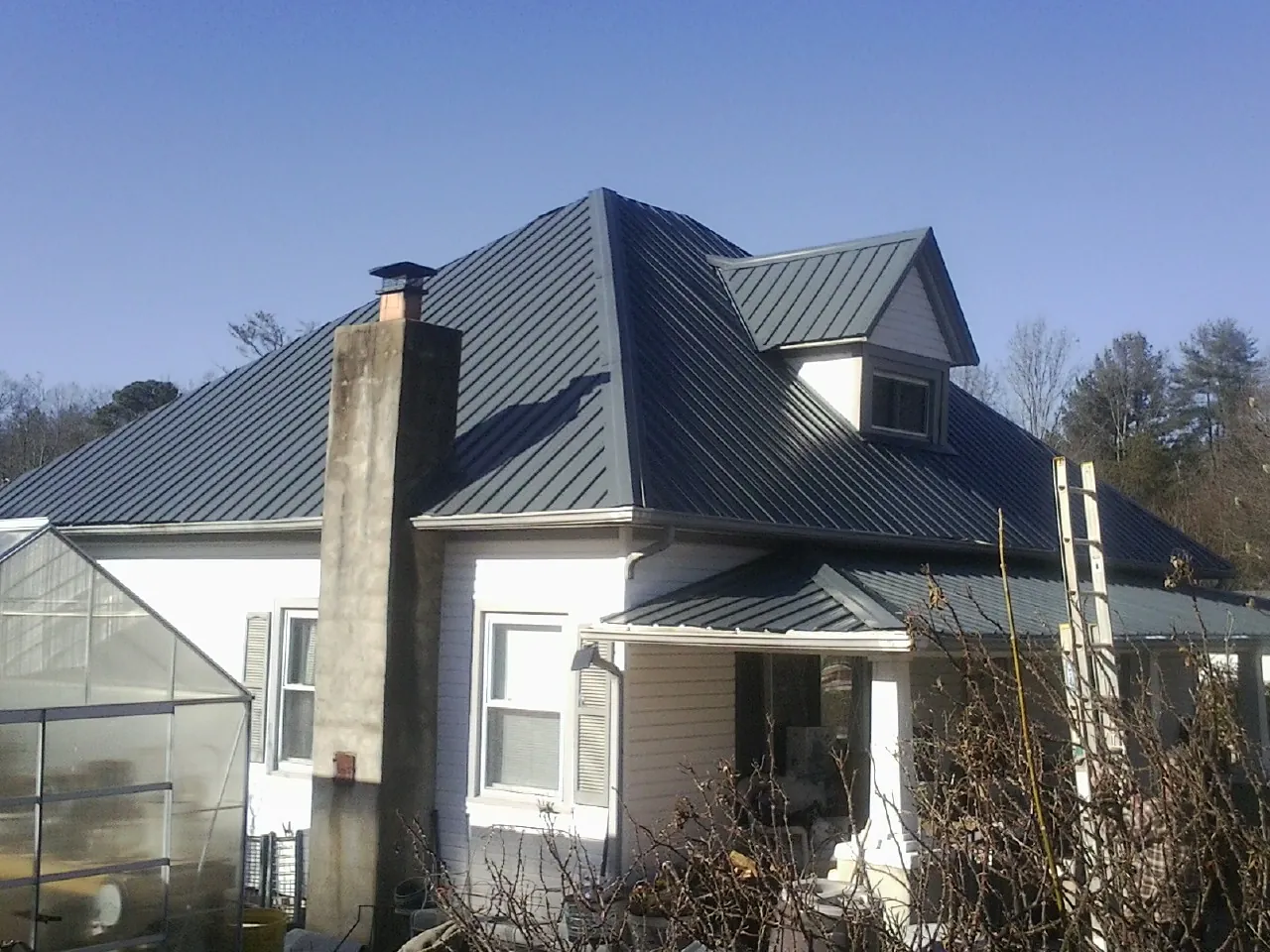 Dark blue standing seam metal roof on a white farmhouse with dormer — Slate & Tile Roof Repair by Roofing Brothers in Lexington Park