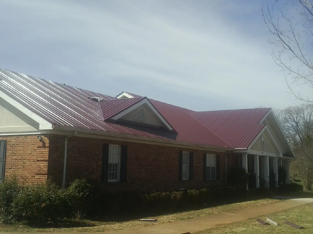 Red metal roof with gabled entries on a long brick building, from a Hail Damage Roof Repair job in Lexington Park