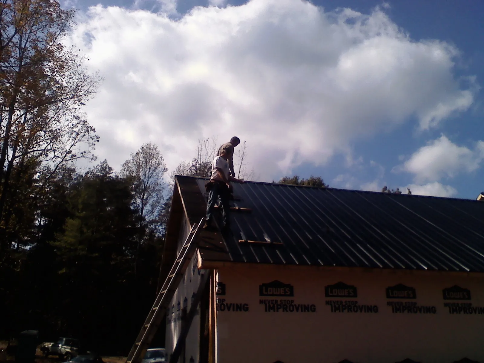 Roofer fastening dark metal panels high against a cloudy sky, from a Roof Inspection job in Lexington Park