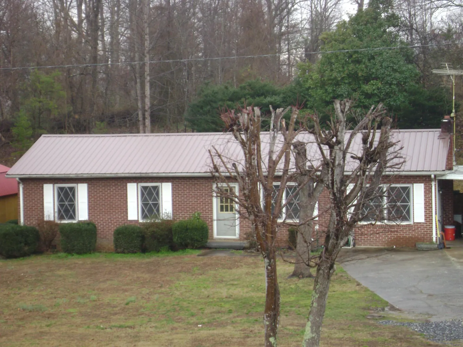 Mauve metal roof on a brick ranch home behind bare trees in Lexington Park