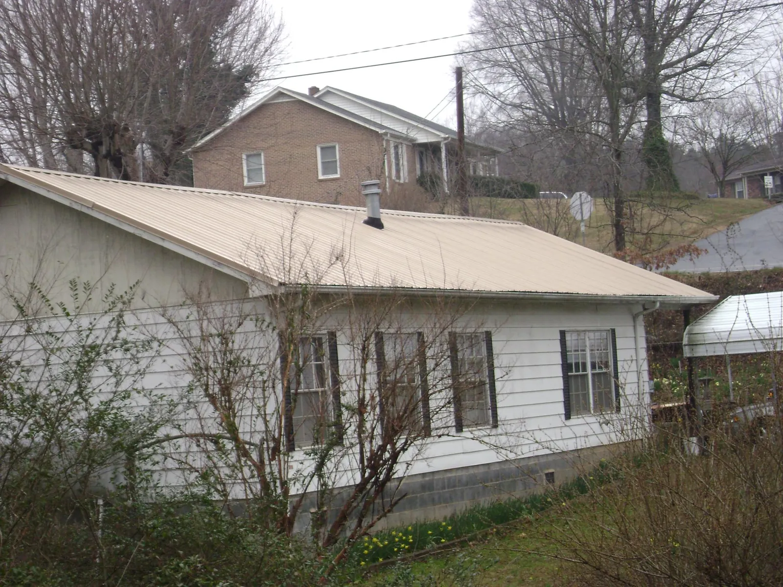 Tan metal roof on a white sided house set into a hillside — Commercial Roofing by Roofing Brothers in Lexington Park